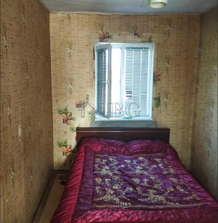 Spacious bedroom featuring vintage wallpaper, a large bed with a colorful quilt, and a window with s.