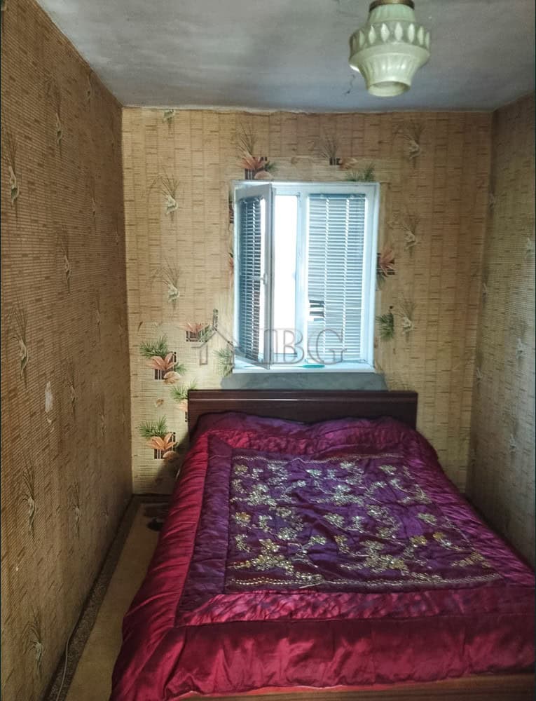 Spacious bedroom featuring vintage wallpaper, a large bed with a colorful quilt, and a window with s.