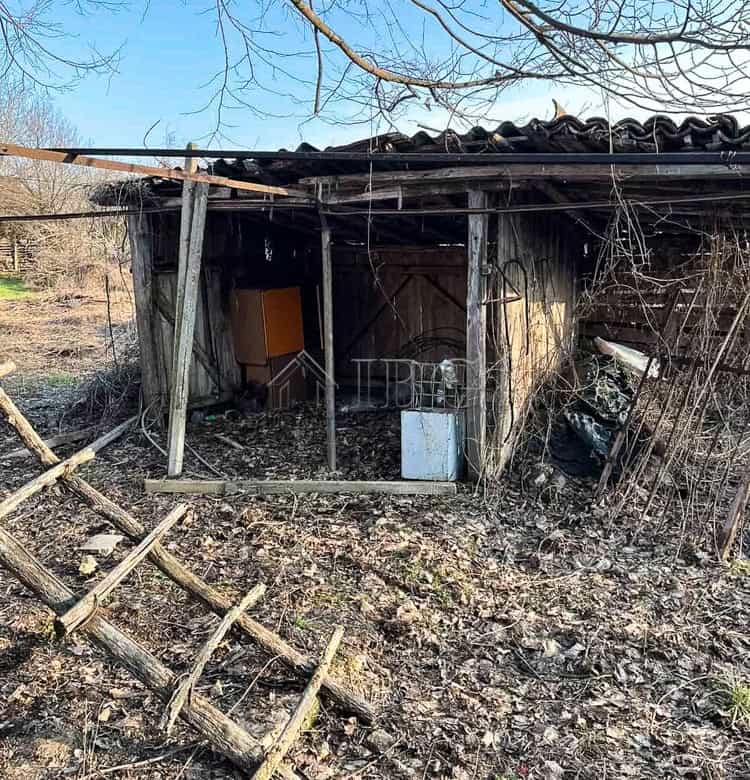 Old wooden shed with a tiled roof, surrounded by a large garden and trees in a rural setting.