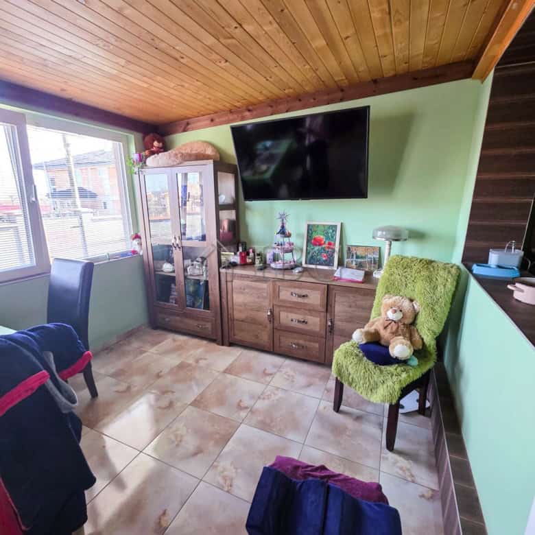 Bright living room with a wall-mounted TV, wooden cabinet, and cozy green armchair with teddy bear.