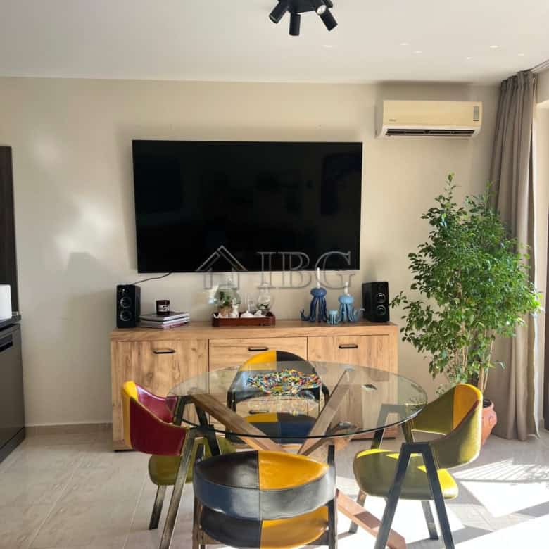 Stylish living space featuring a large flat-screen TV, colorful dining chairs, and natural sunlight.