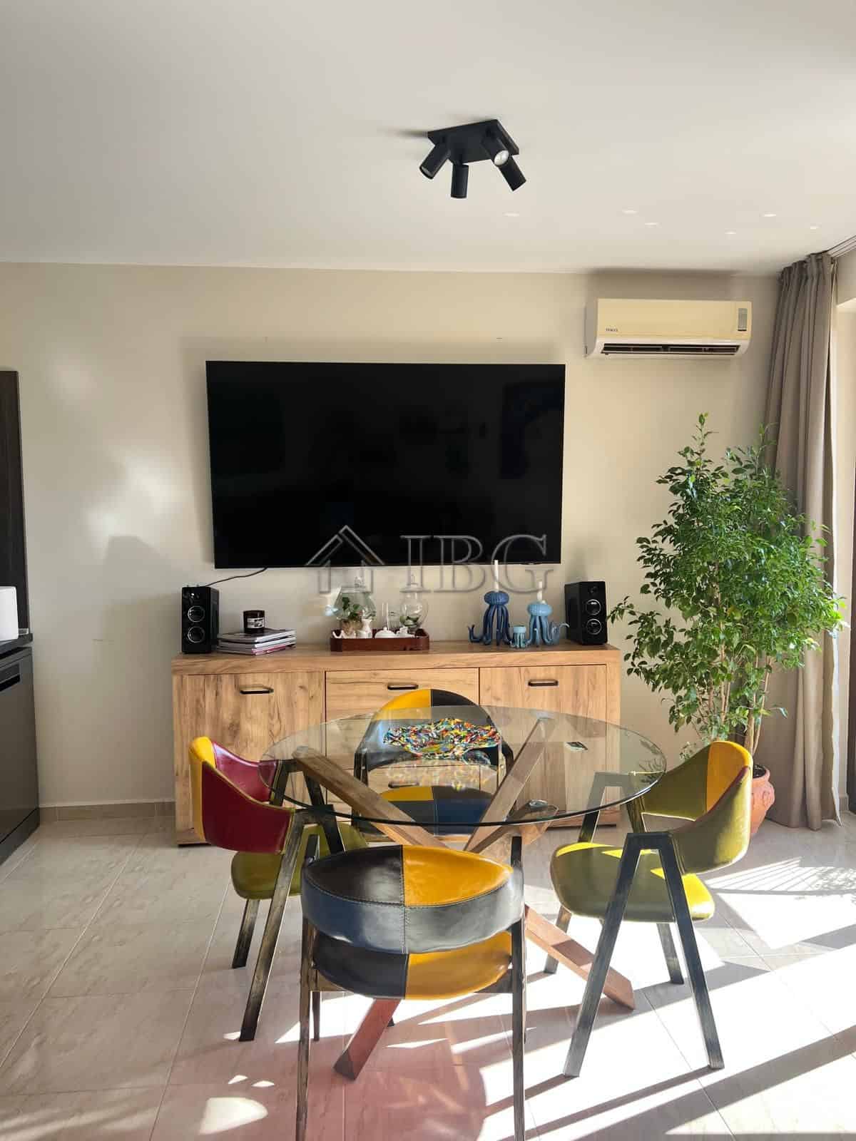 Stylish living space featuring a large flat-screen TV, colorful dining chairs, and natural sunlight.