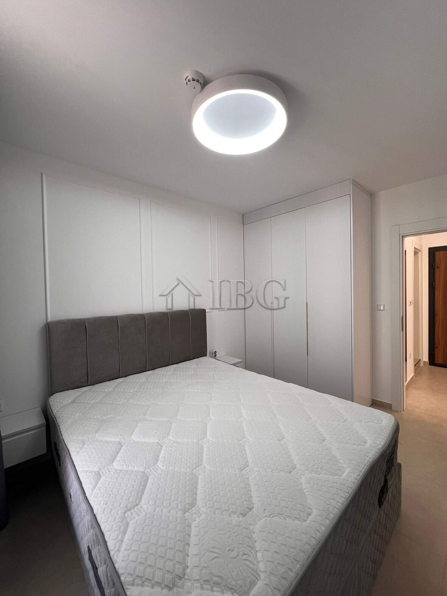 Bright bedroom with white walls, gray headboard, and modern ceiling light fixture.