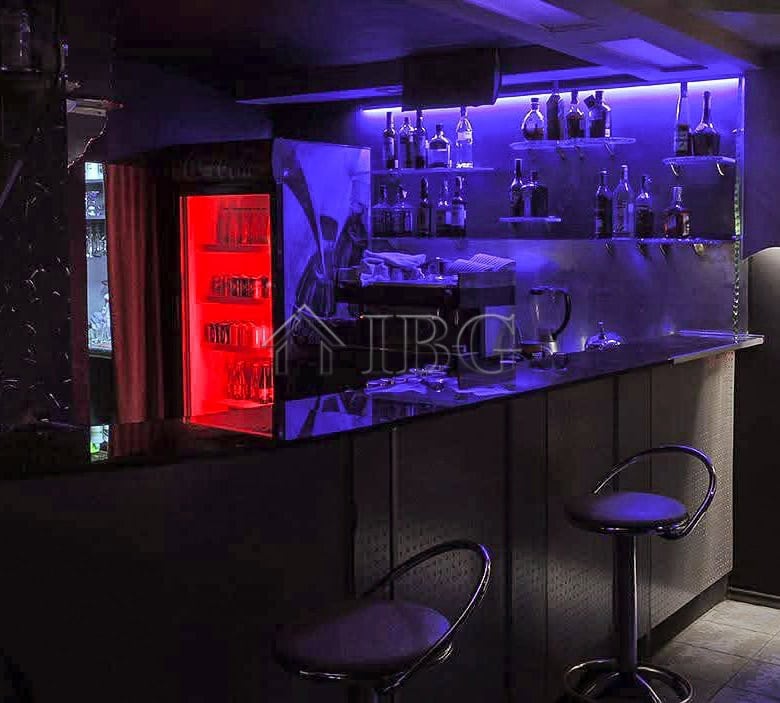 Bar with illuminated shelves and seating in a commercial premises.