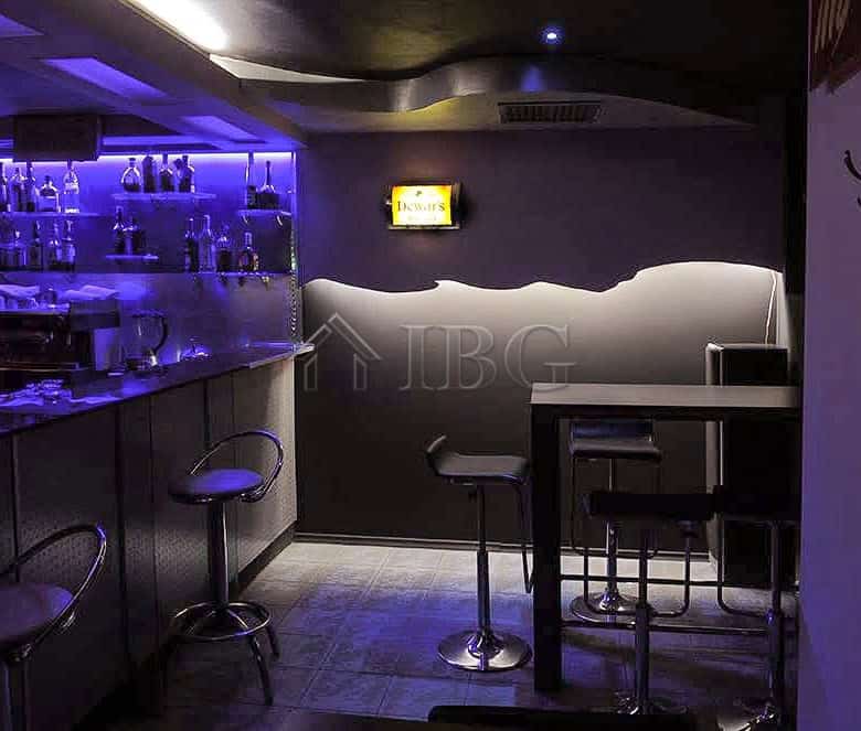 Interior view of a modern commercial premises featuring a bar counter, illuminated shelves, and seat.