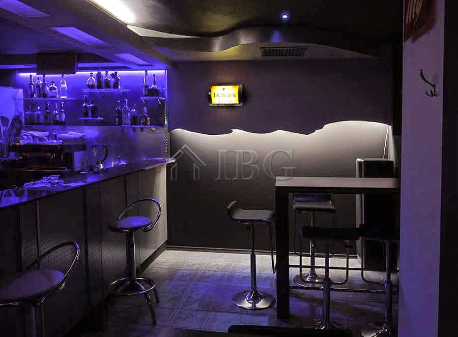 Interior view of a modern commercial premises featuring a bar counter, illuminated shelves, and seat.