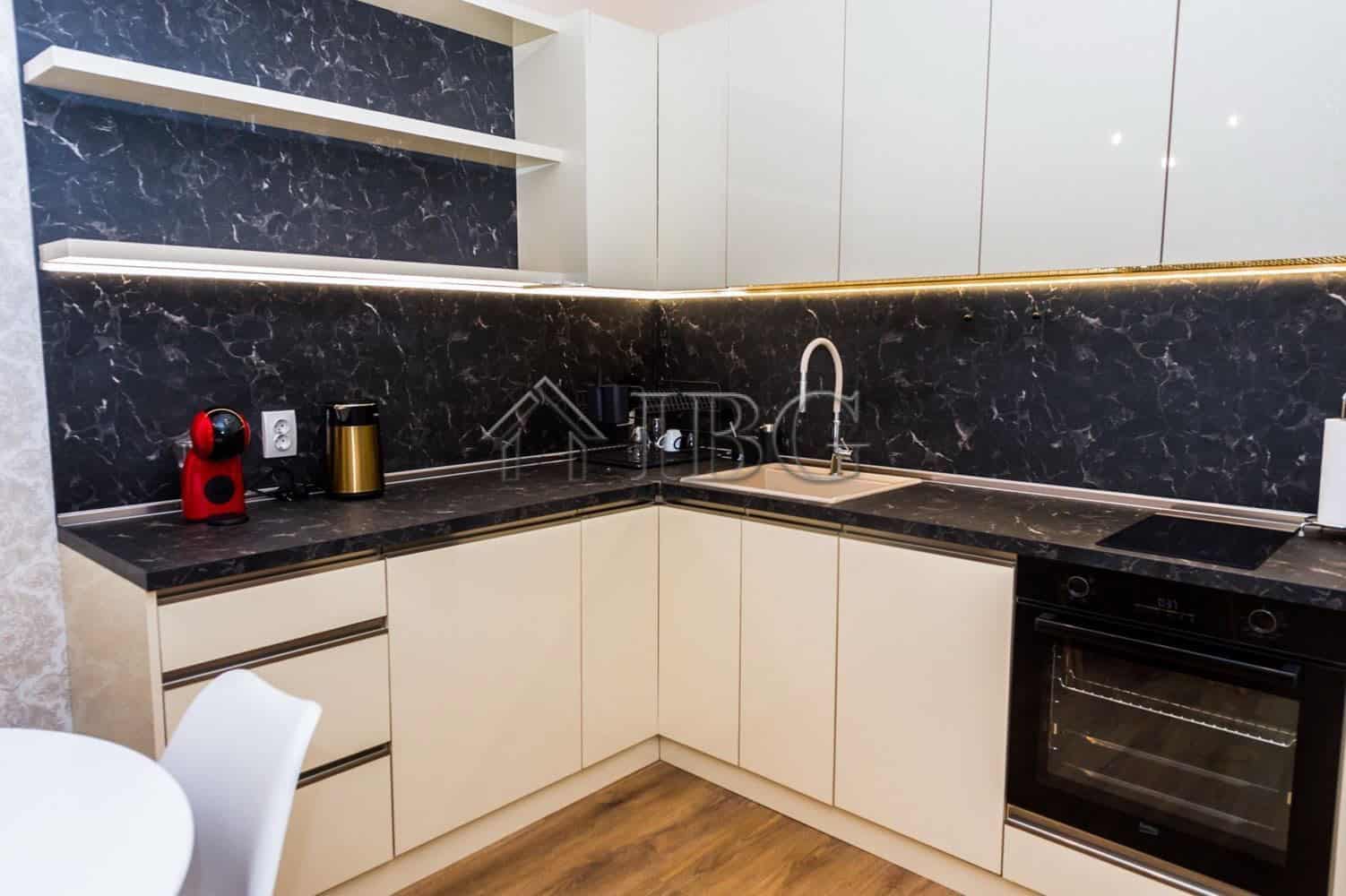 Modern kitchen with black marble countertops and white cabinetry in Lazur District, Burgas.