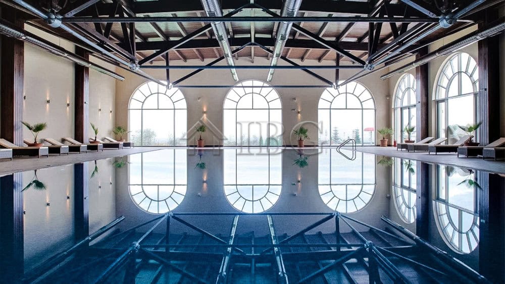 Indoor swimming pool with large arched windows and stylish decor.