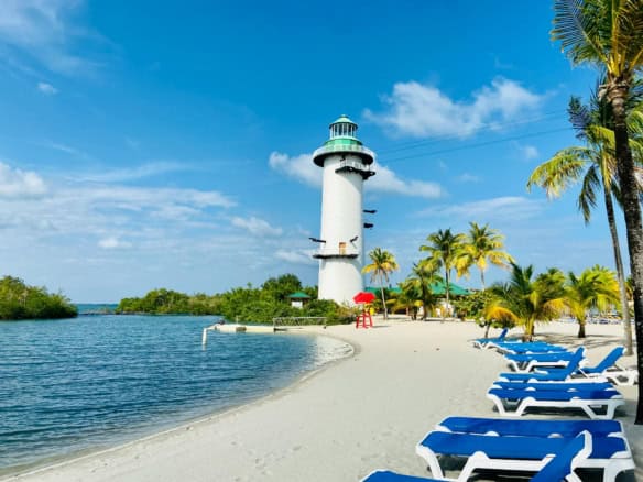 Lighthouse on Belizean beach with palm trees and lounge chairs, perfect for relaxing and enjoying co.