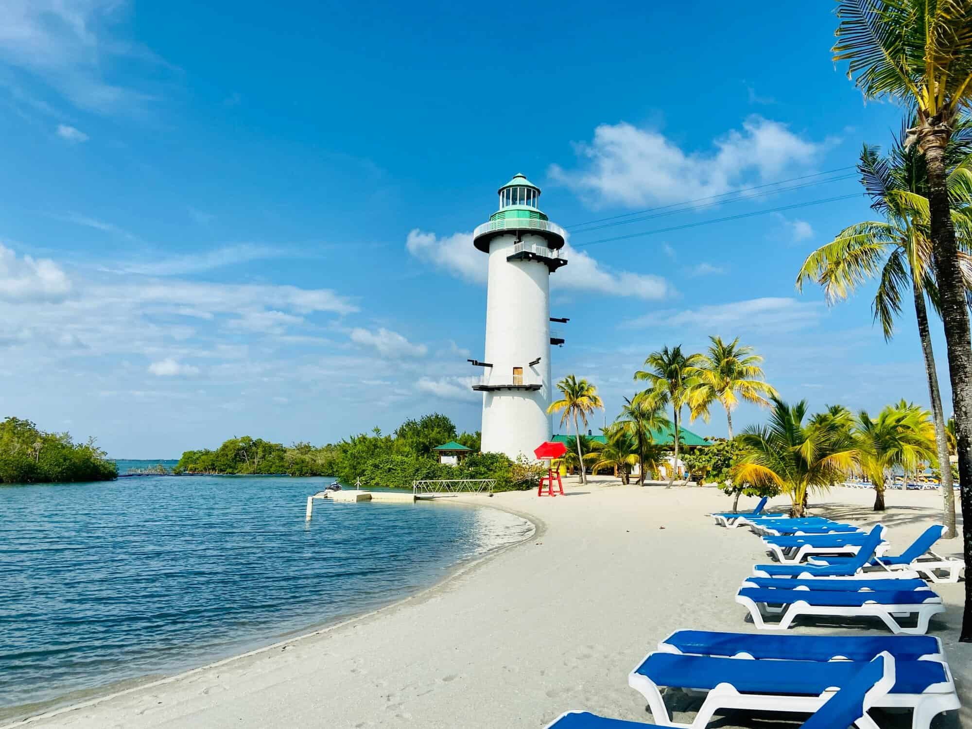 Lighthouse on Belizean beach with palm trees and lounge chairs, perfect for relaxing and enjoying co.