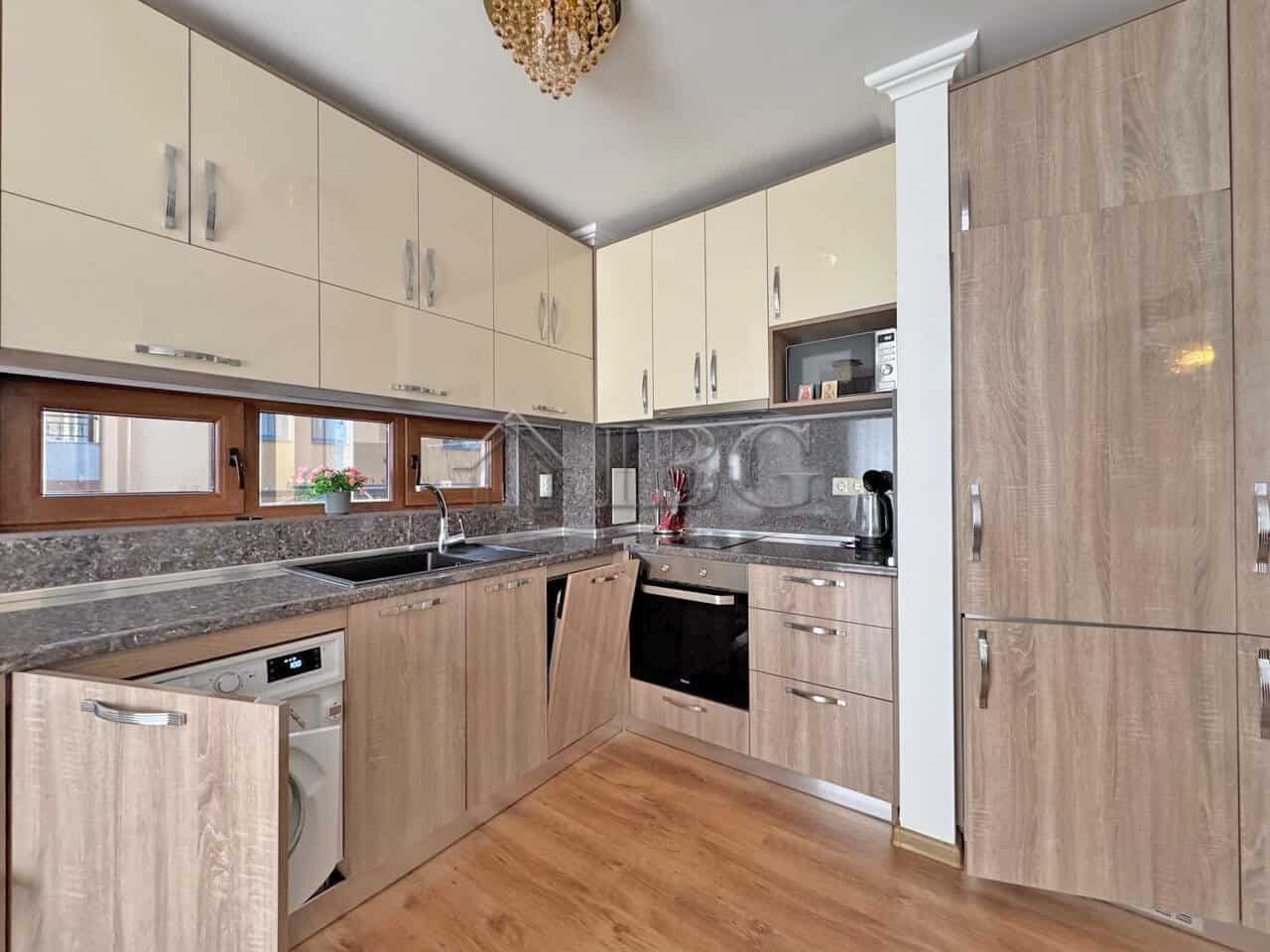 Modern kitchen with wooden cabinets, sink, oven, and washing machine.