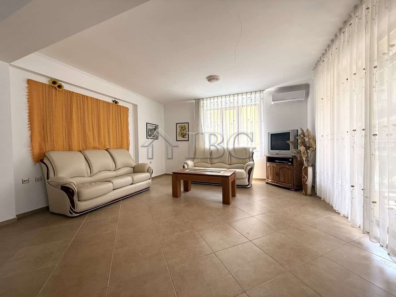 Bright living room with large windows and comfortable seating in Tili Complex, Aurelia District, Nes.
