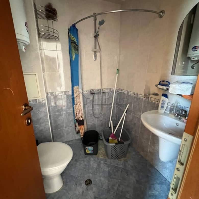 Apartment bathroom with shower, toilet, and sink in Sunny Beach. Compact space with cleaning supplie.