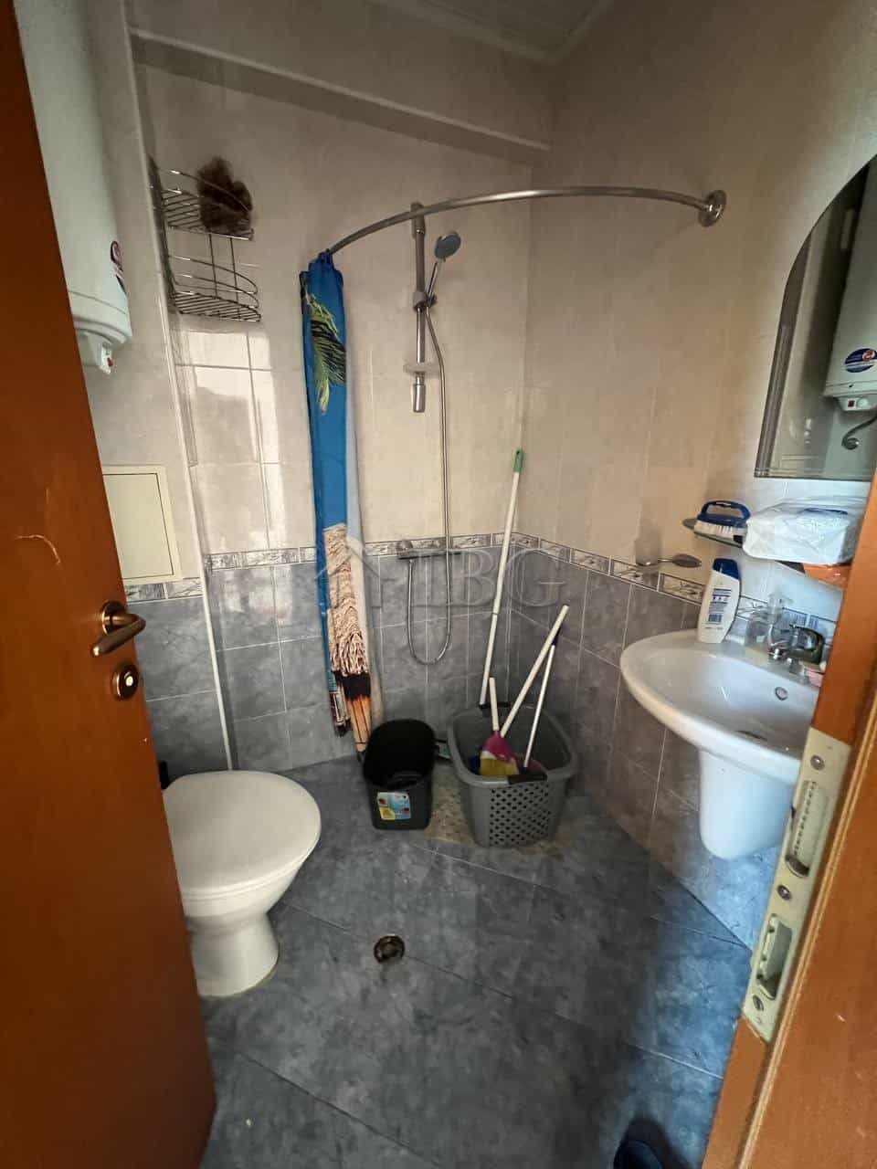Apartment bathroom with shower, toilet, and sink in Sunny Beach. Compact space with cleaning supplie.