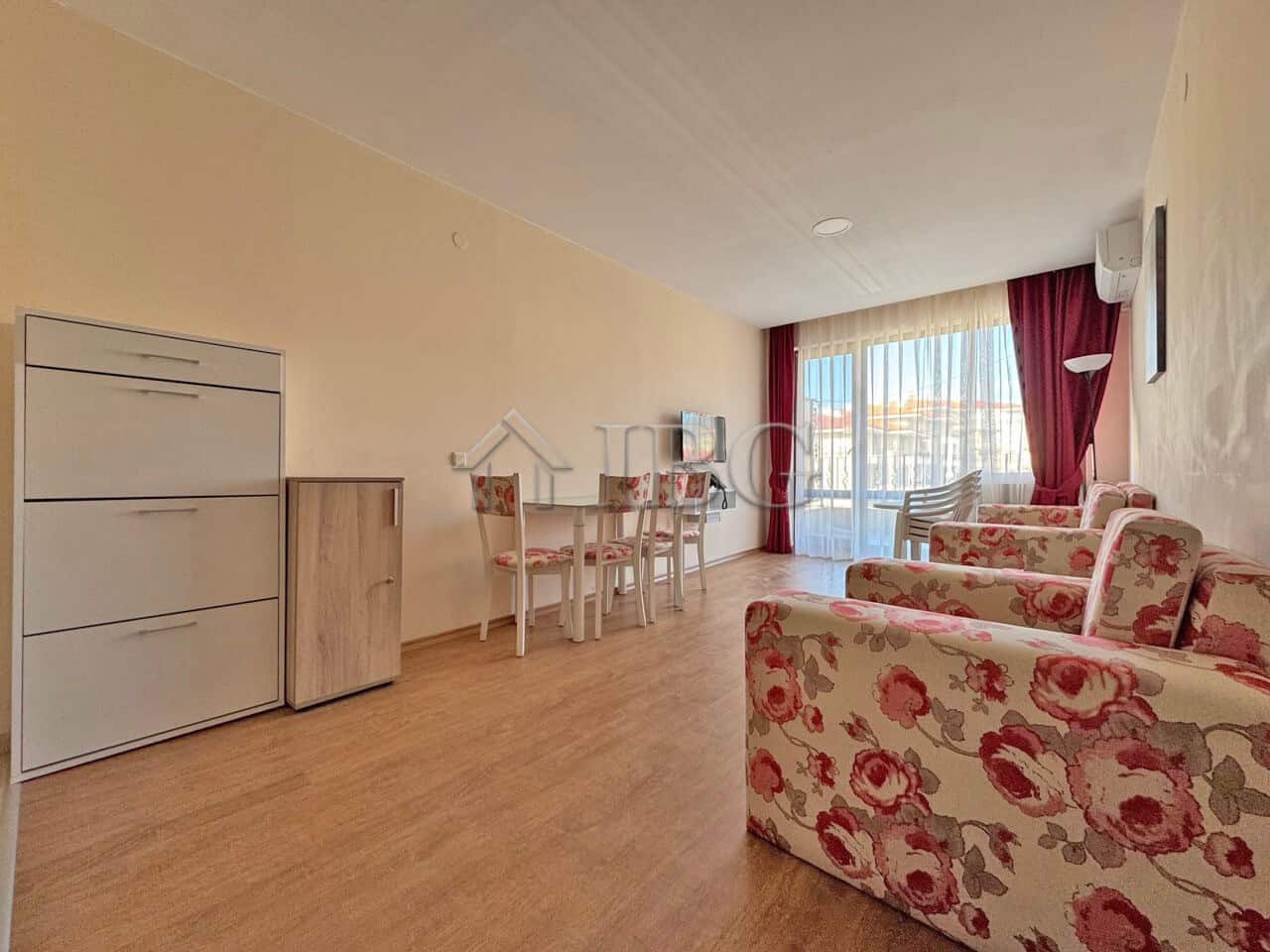 Apartment (1+1) for Sale | Premier Fort Beach, Sveti Vlas Bright living room with large windows and floral sofas.