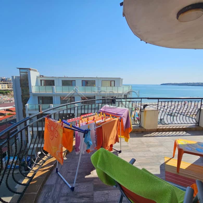 Bright sea view balcony with laundry drying rack and outdoor seating.