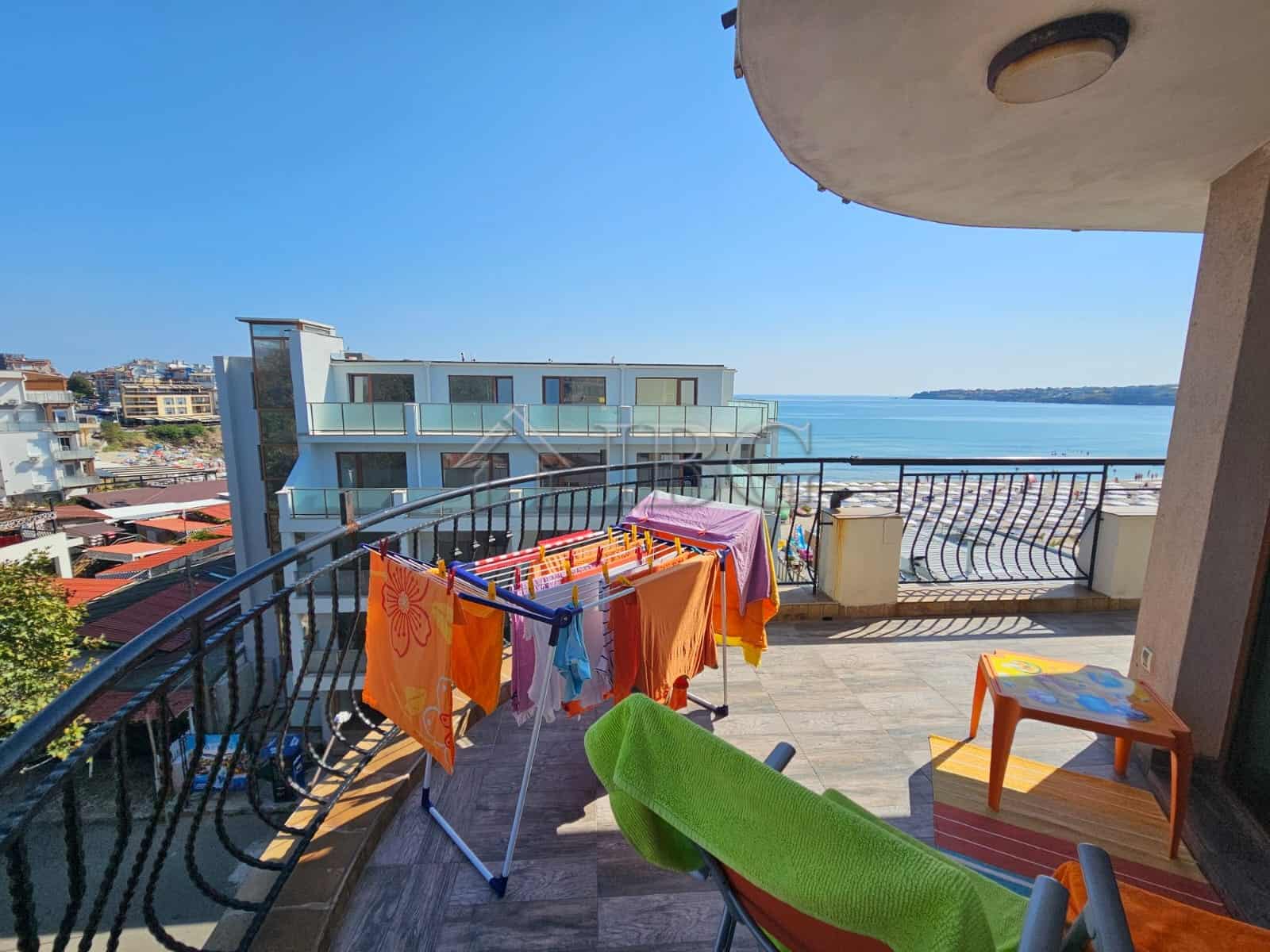 Bright sea view balcony with laundry drying rack and outdoor seating.