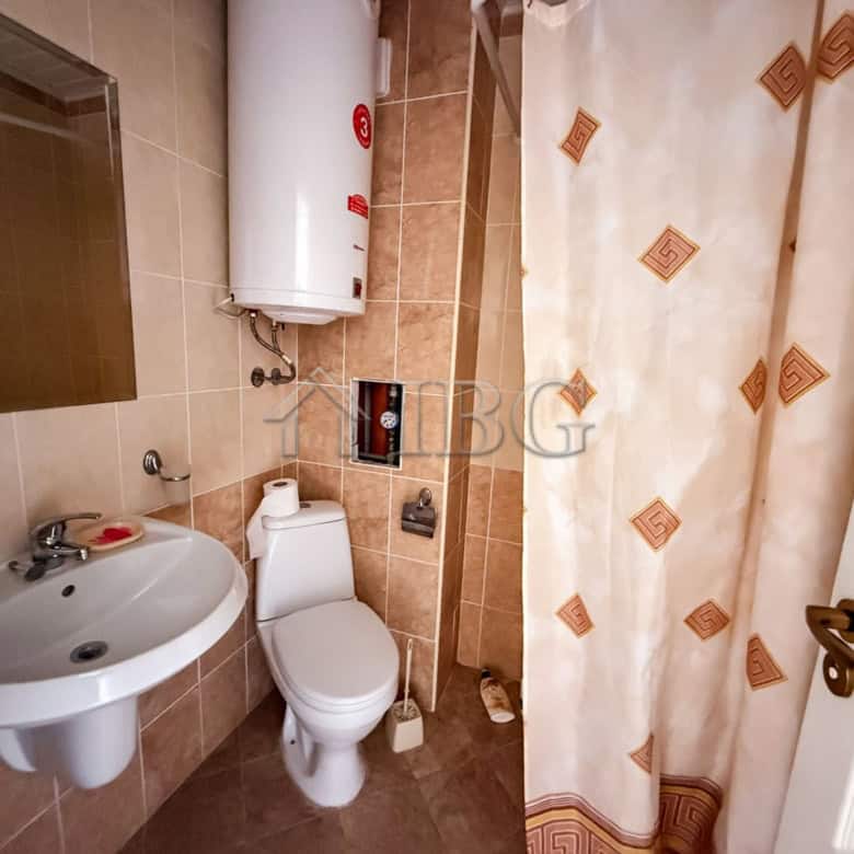 Small bathroom with sink, toilet, and shower curtain in a sunny beach studio apartment.