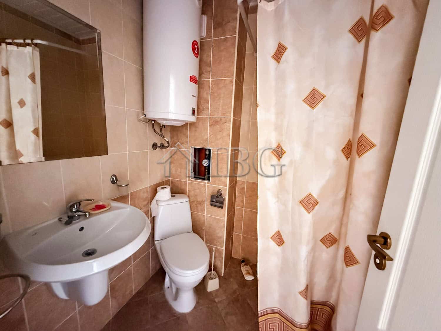 Small bathroom with sink, toilet, and shower curtain in a sunny beach studio apartment.