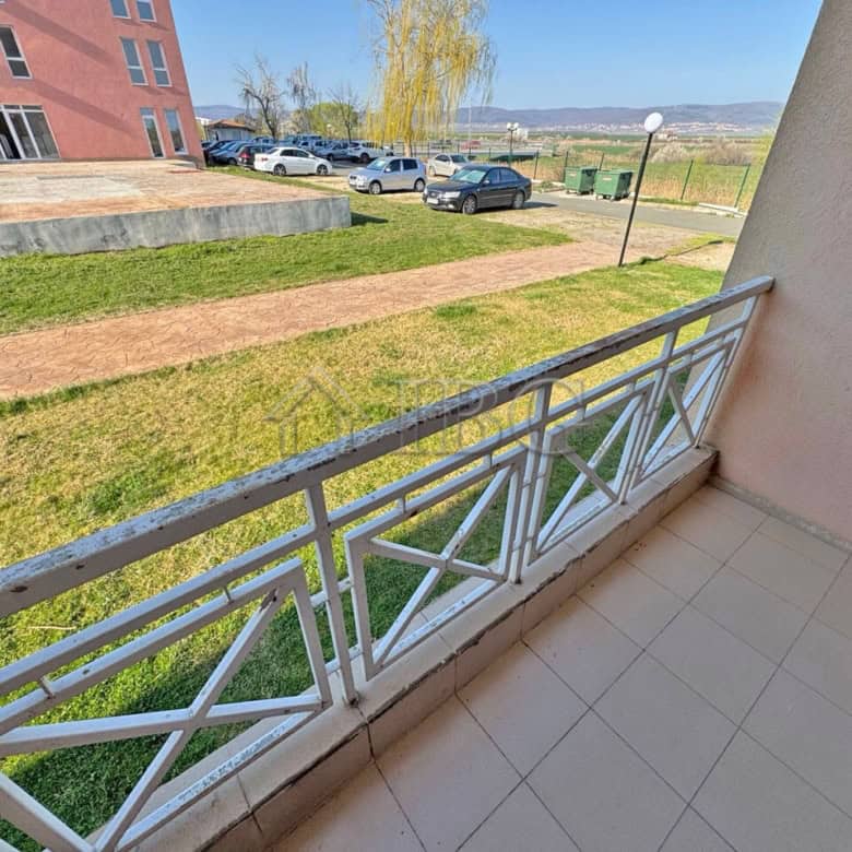 Ground-floor apartment with balcony overlooking green yard and parking area.