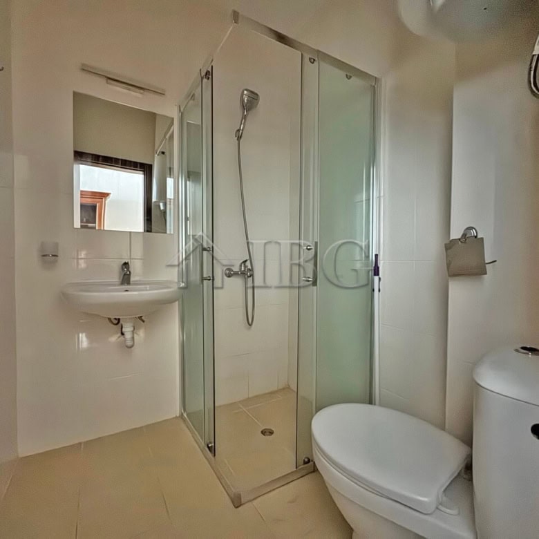 Compact bathroom with shower enclosure, toilet, and sink in a sunny studio apartment.