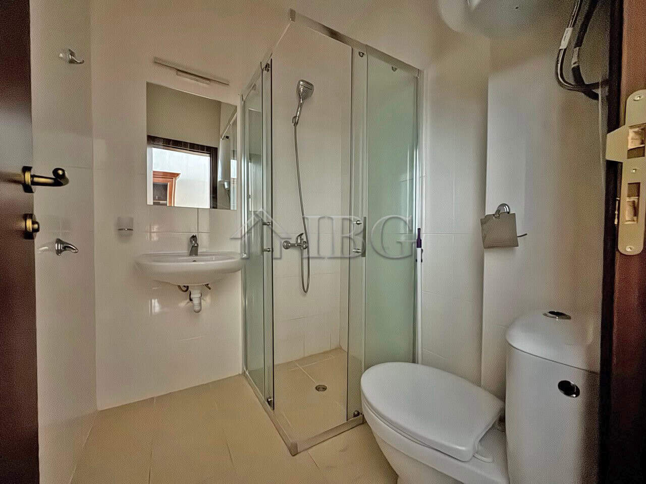 Compact bathroom with shower enclosure, toilet, and sink in a sunny studio apartment.