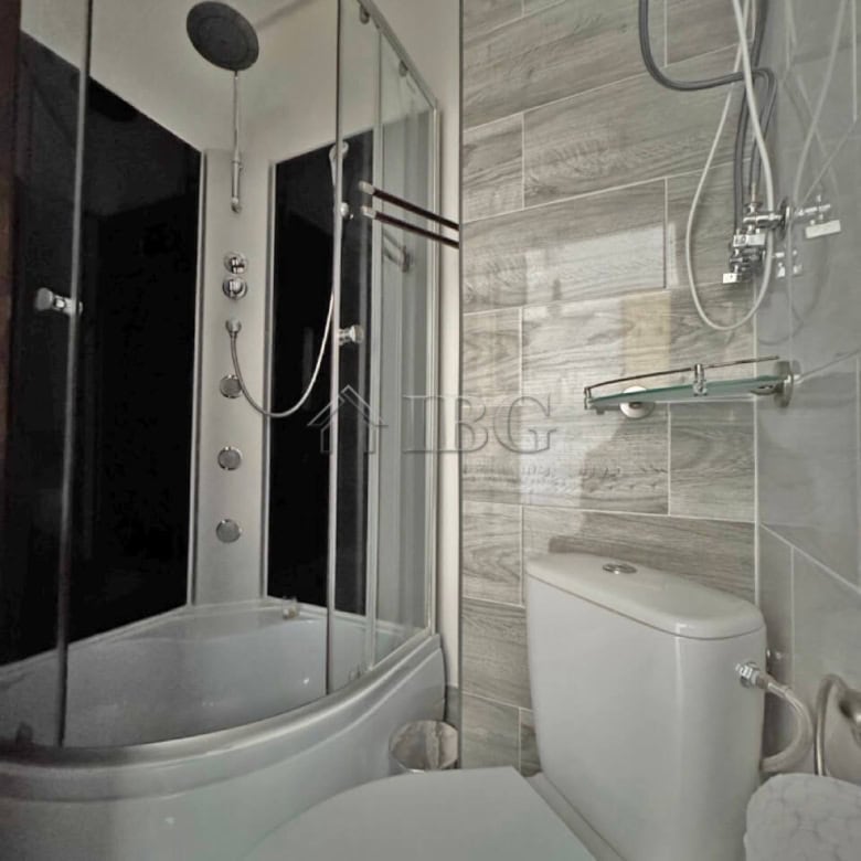 Furnished studio with modern shower cabin, toilet, and wall-mounted shower head. Compact bathroom in.
