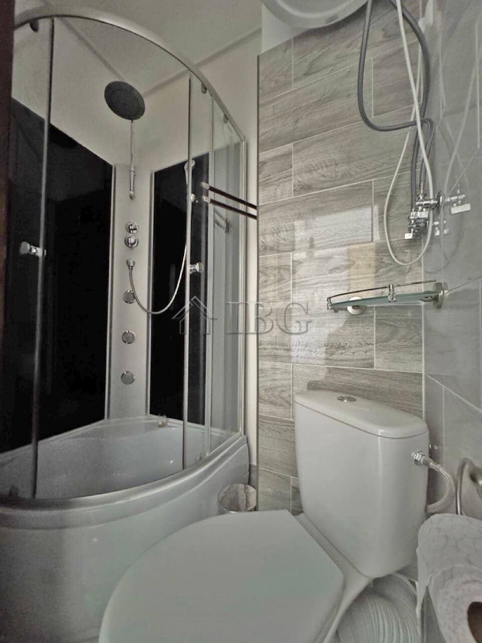Furnished studio with modern shower cabin, toilet, and wall-mounted shower head. Compact bathroom in.