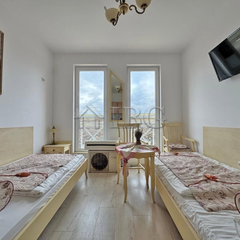 Furnished studio apartment with two single beds, bright interior, and large windows overlooking Sunn.
