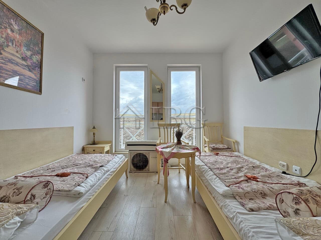 Furnished studio apartment with two single beds, bright interior, and large windows overlooking Sunn.