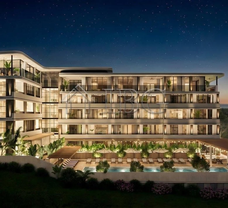 Night view of Loggia Residences near the sea with illuminated balconies and lush surroundings.