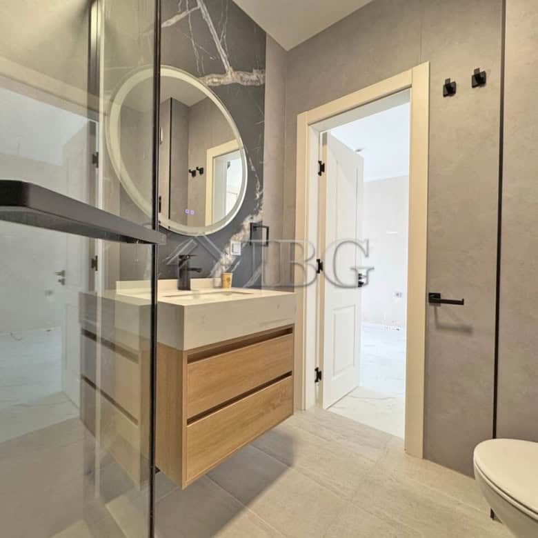 Bright bathroom featuring a wooden vanity, round mirror, and modern fixtures in a sunny beach proper.