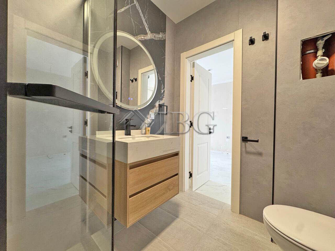 Bright bathroom featuring a wooden vanity, round mirror, and modern fixtures in a sunny beach proper.
