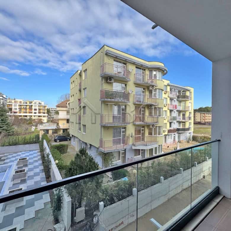 Bright yellow one-bedroom apartment with balcony overlooking neighboring buildings and greenery.