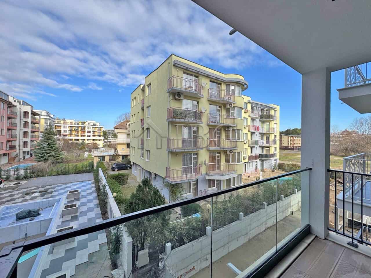 Bright yellow one-bedroom apartment with balcony overlooking neighboring buildings and greenery.