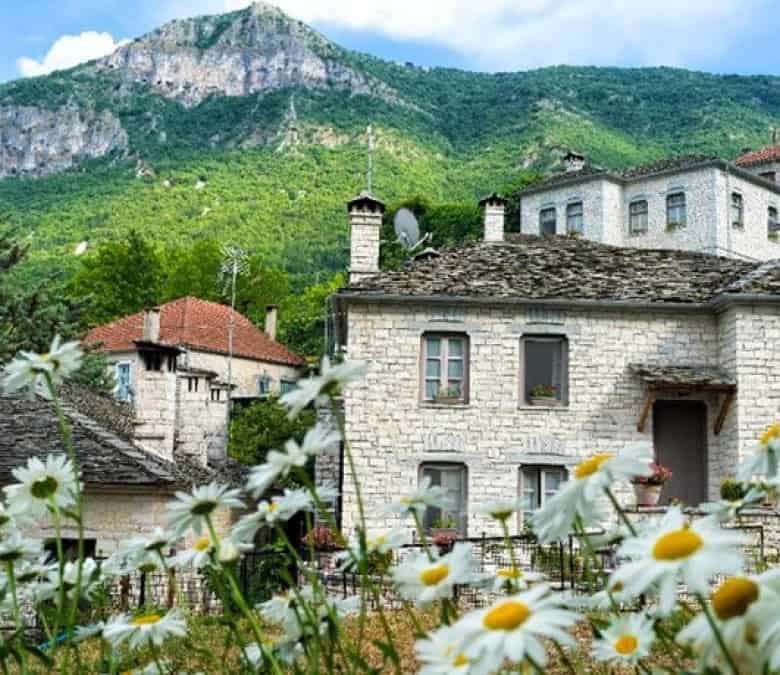 Beautiful stone houses in Vitsa, Zagori, Greece, with lush green mountains in the background.