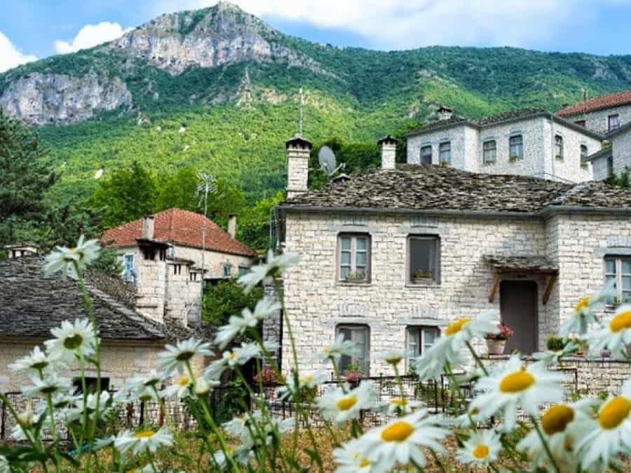 Beautiful stone houses in Vitsa, Zagori, Greece, with lush green mountains in the background.
